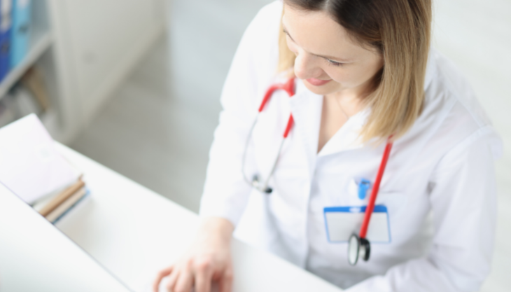 A female doctor smiling while using a HIPAA-compliant messaging app on her computer.