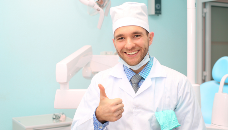 A male dentist gesturing a thumbs up.