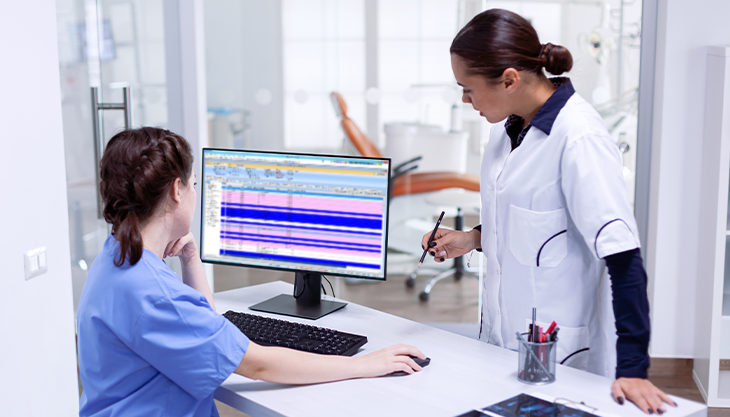 Two healthcare workers navigating their practice management software from a desktop computer..