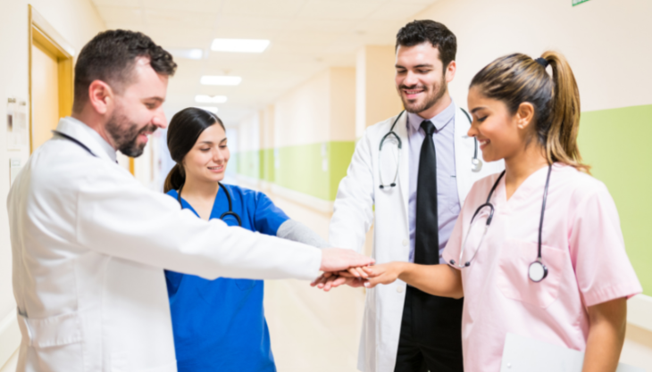 Four healthcare workers huddling and putting their hands together, signifying strong provider-to-provider communication.