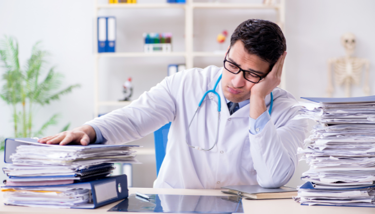 Allergist looks defeatedly at clinic paperwork on his desk.