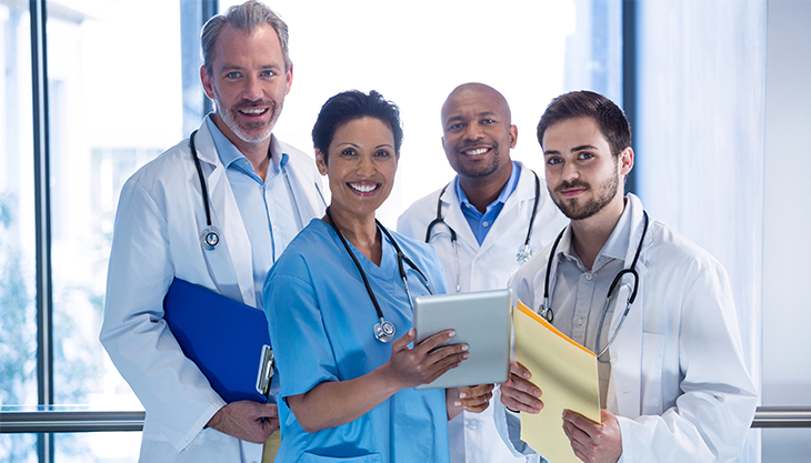 Four medical doctors of different specialties huddled in a hospital hallway.