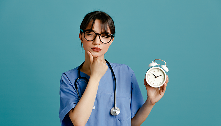 A healthcare professional holding up an alarm clock with visible wonder in her face.