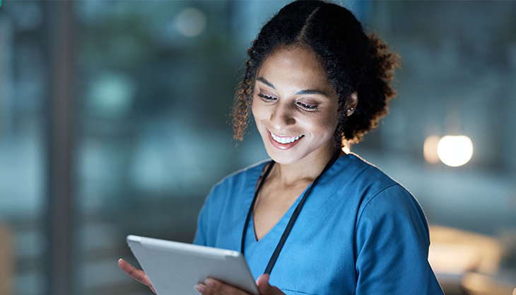 A female healthcare worker smiling while using a tablet.