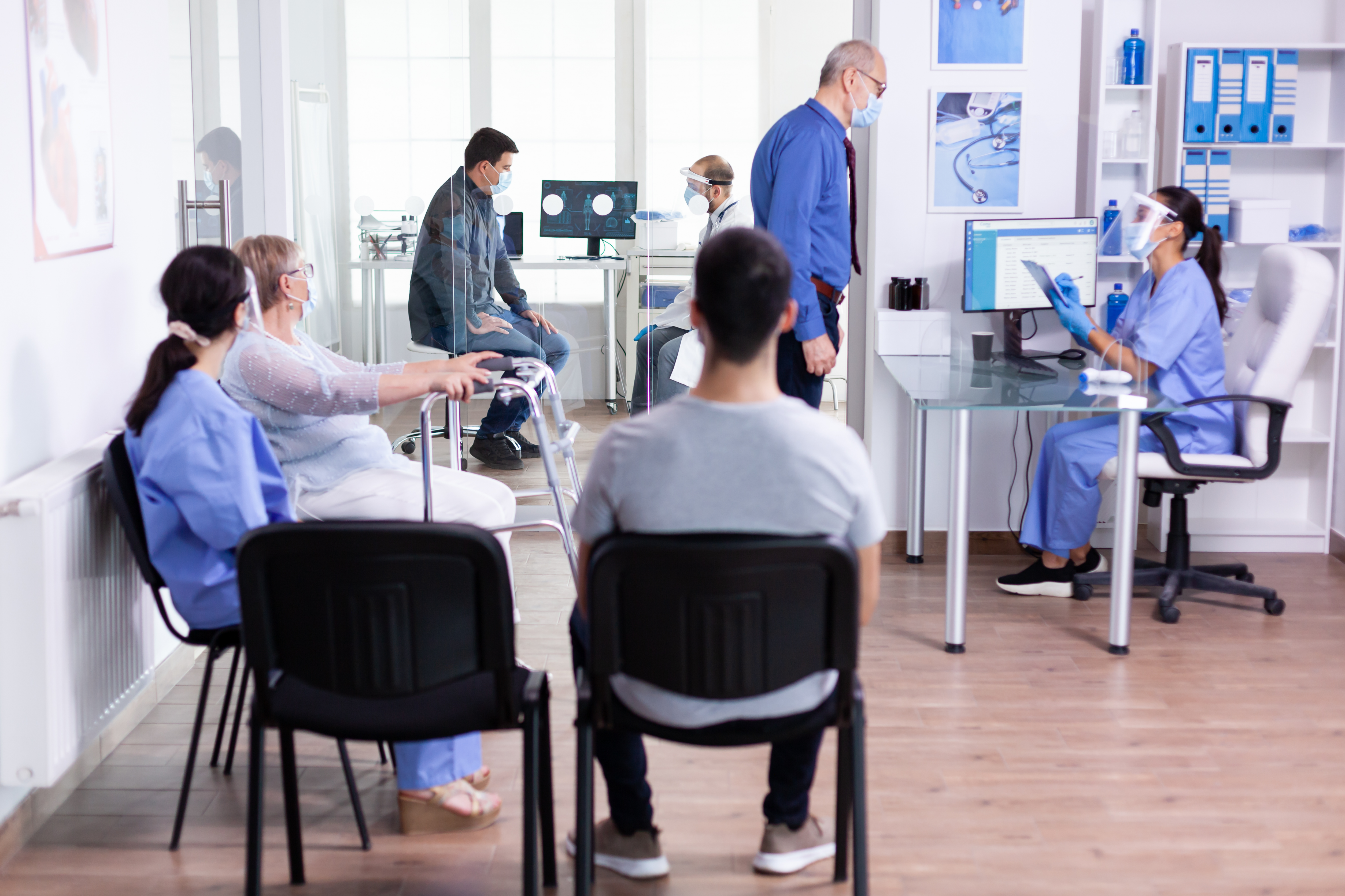 In a busy healthcare clinic, a patient attends a consultation with their doctor while other patients wait for their turn in the waiting room. 