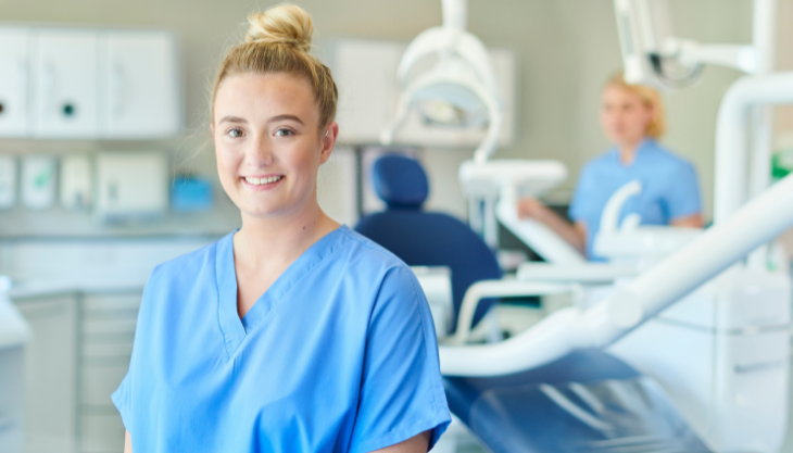 A female dental professional posing for the camera with her colleague in the background.