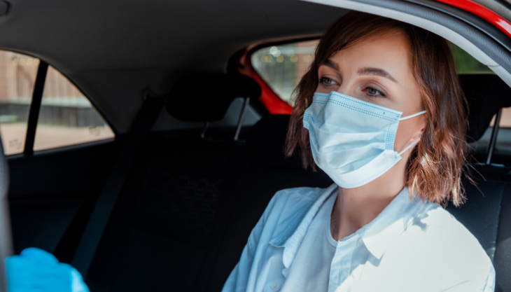 Woman with a mask sitting in the back of a non-medical transportation uber 
